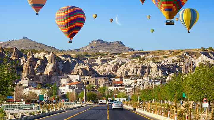 Hot air balloons fly over the Goreme road at sunrise in Cappadocia